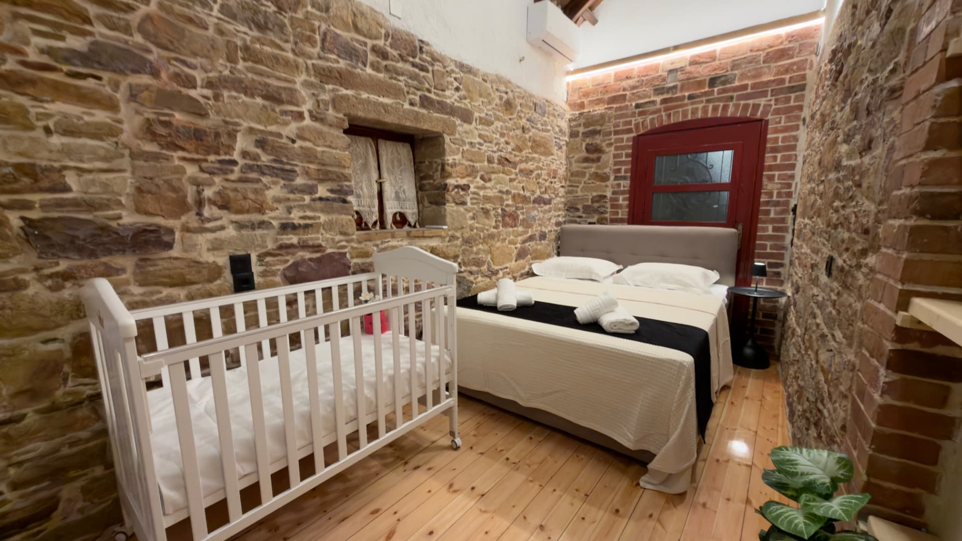Bedroom with stone wall, bed with white linen and a baby cot