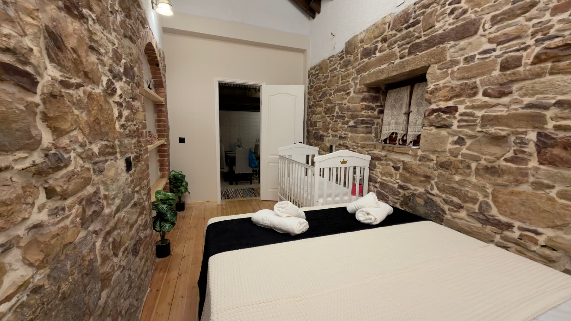 Bedroom with stone walls, bed with towels and a white baby cot