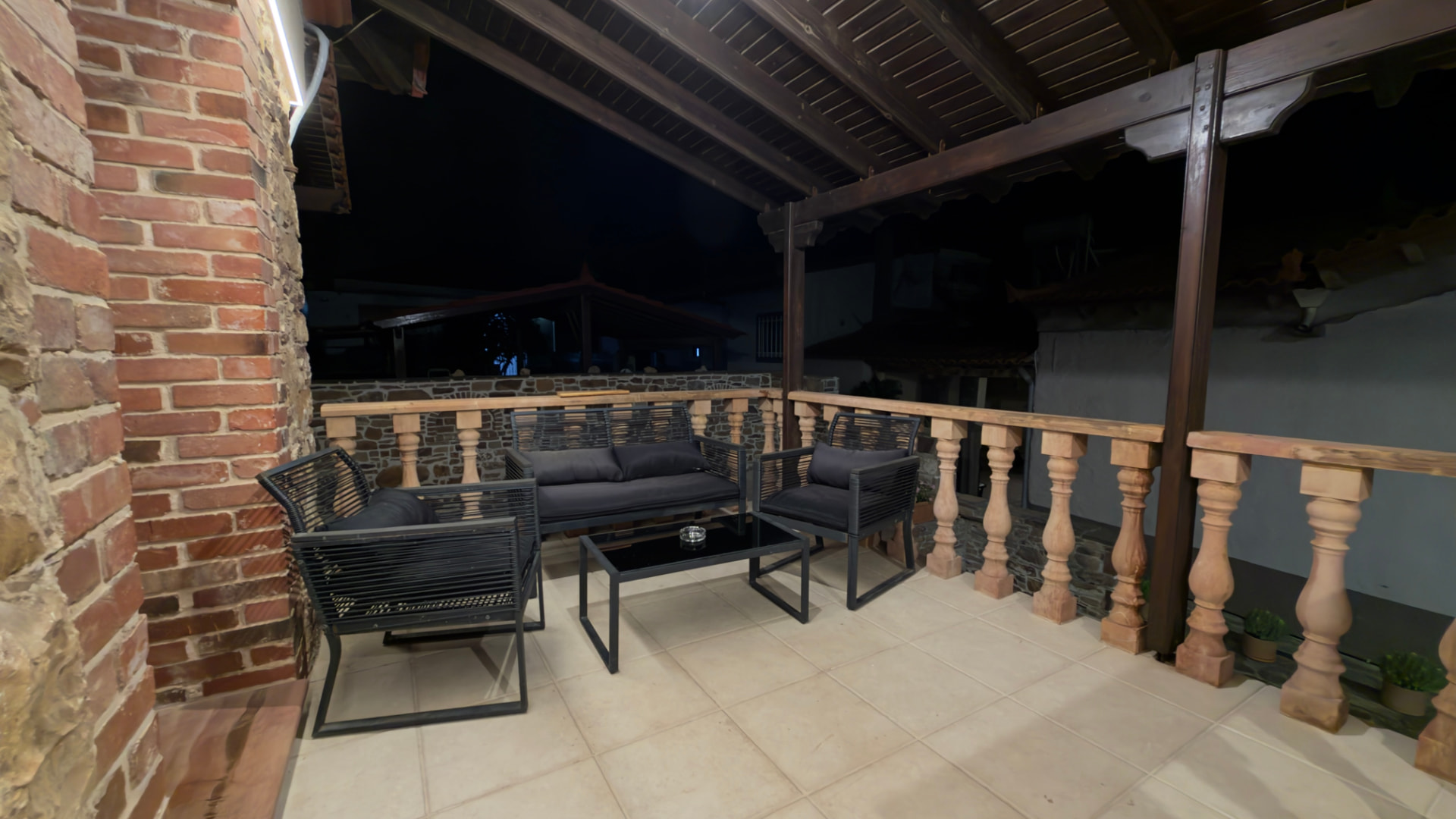 Covered terrace with timber roof, sofa and armchairs next to a stone wall