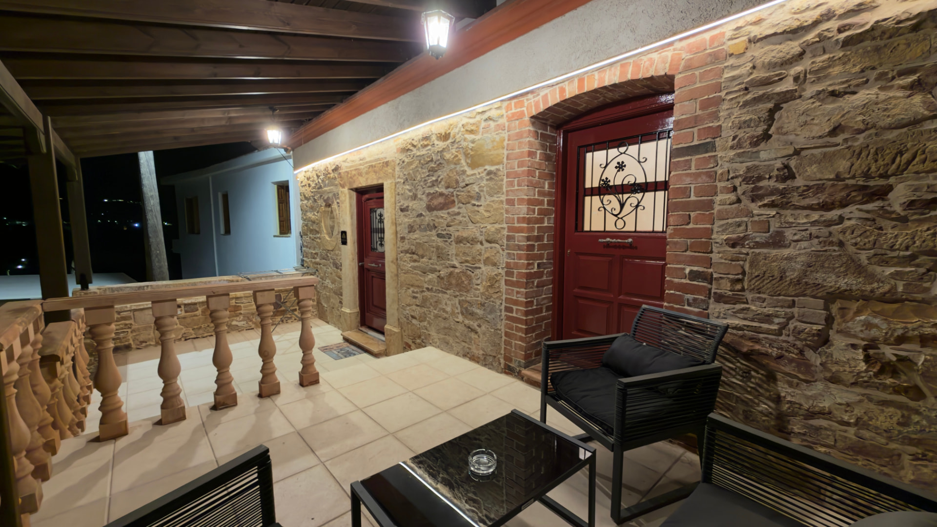 Stone wall with a red wooden door and lighting, with the terrace seating in front