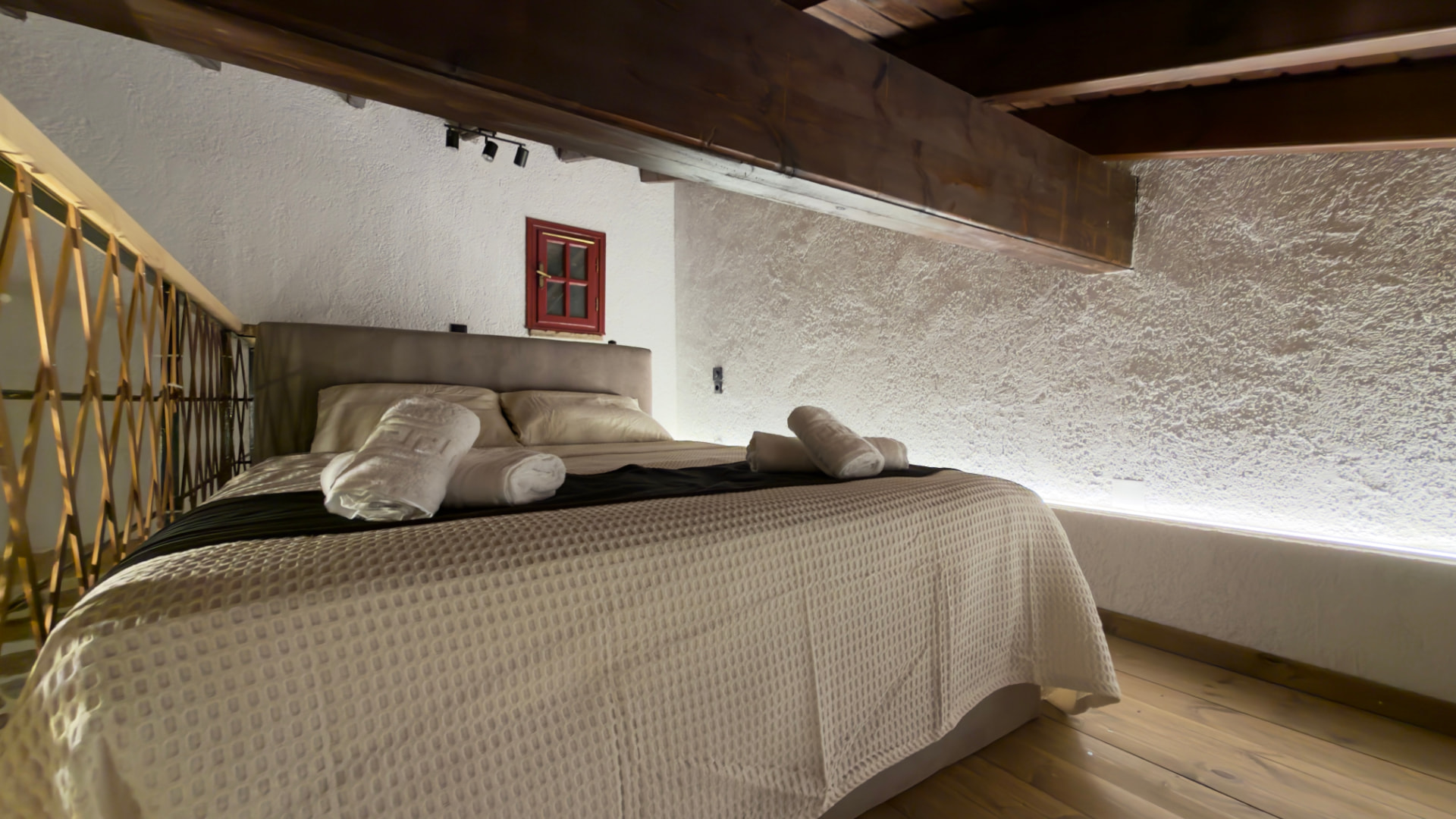 Loft with bed, wooden railing and an illuminated stone wall
